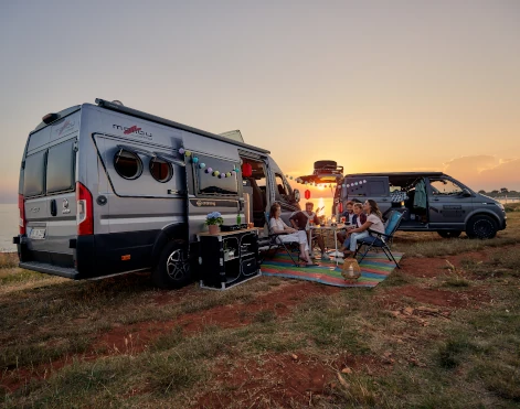 Camper vor zwei Vans in abendlicher Atmosphäre an einem See