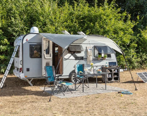 Wohnwagen mit diversen Camping-Möbeln, einem Solarpanel und einem Sonnendach